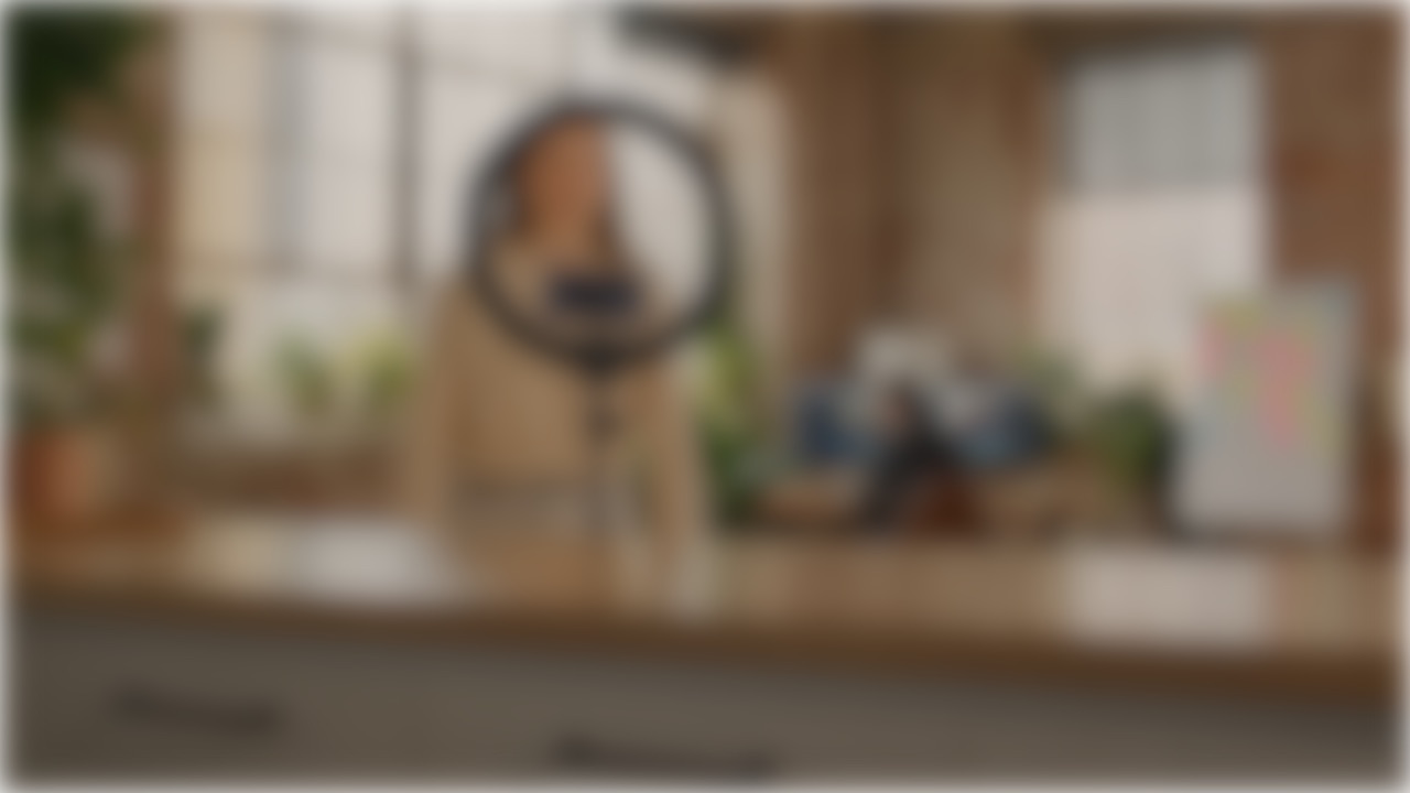 A soft-focus view of a shoot set: a ring light on a counter, plants, an editor's desk behind